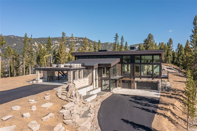 Rustic wooden cabin in a snowy mountain landscape with trees and blue sky.